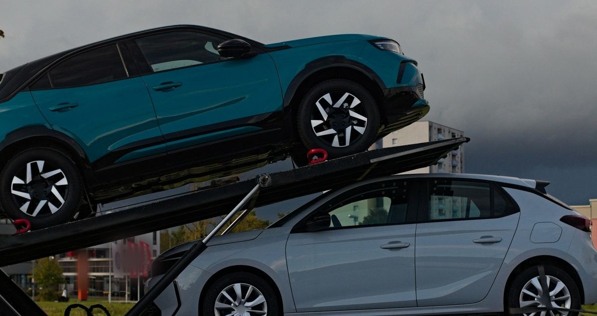 Twee wagens op een autotransporter, een blauwgroene en een zilveren