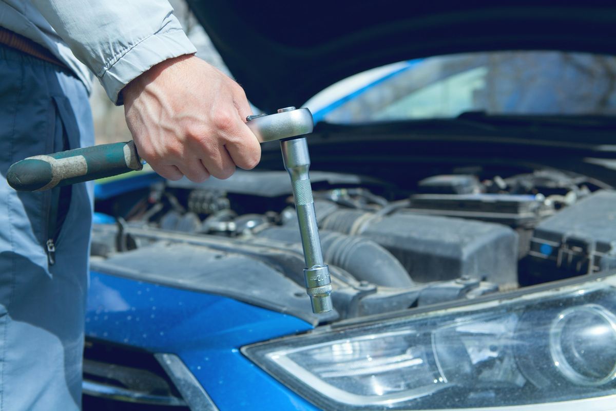 Een hand met een ratelsleutel boven de open motorruimte van een blauwe wagen